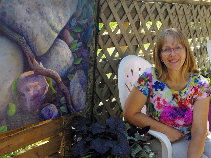 Judy sitting in her garden beside a painting of rocks